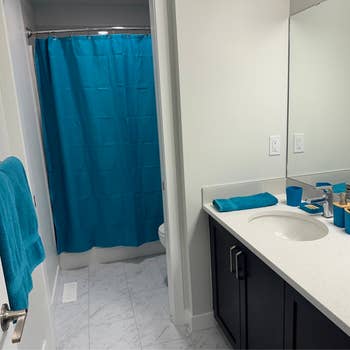 Bathroom with a blue shower curtain and towel, dark vanity with a white countertop, and accessories neatly arranged