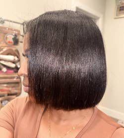 Black reviewer with sleek, straight bob haircut wearing a simple necklace and casual top, standing indoors