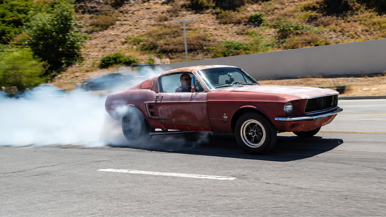 Rusty '67 fastback Mustang shredding tire in the street