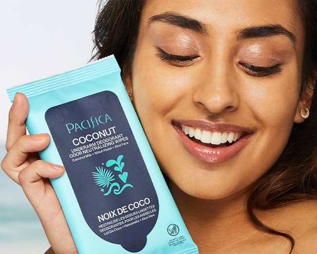 model smiling while holding a pack of Pacha coconut milk deodorant wipes, advertised as gentle and refreshing for on-the-go use