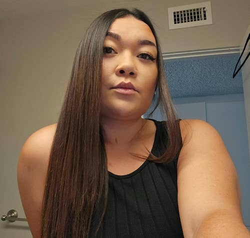 Person with long hair wearing a sleeveless black top in a room with a neutral background