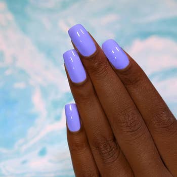 Hand with glossy, square-shaped nails displayed against a marbled background, showcasing a chic manicure style