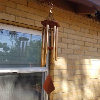 Wind chimes hanging on a porch near a window, casting shadows on a brick wall