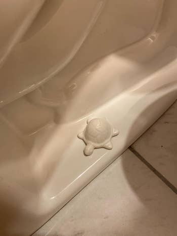 White ceramic turtle figurine placed on a bathroom toilet bolt