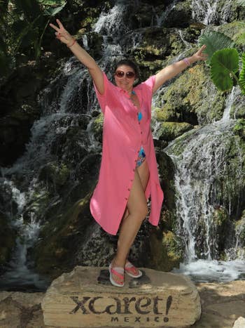 Person in a casual beach outfit poses with arms raised near a waterfall in Xcaret, Mexico