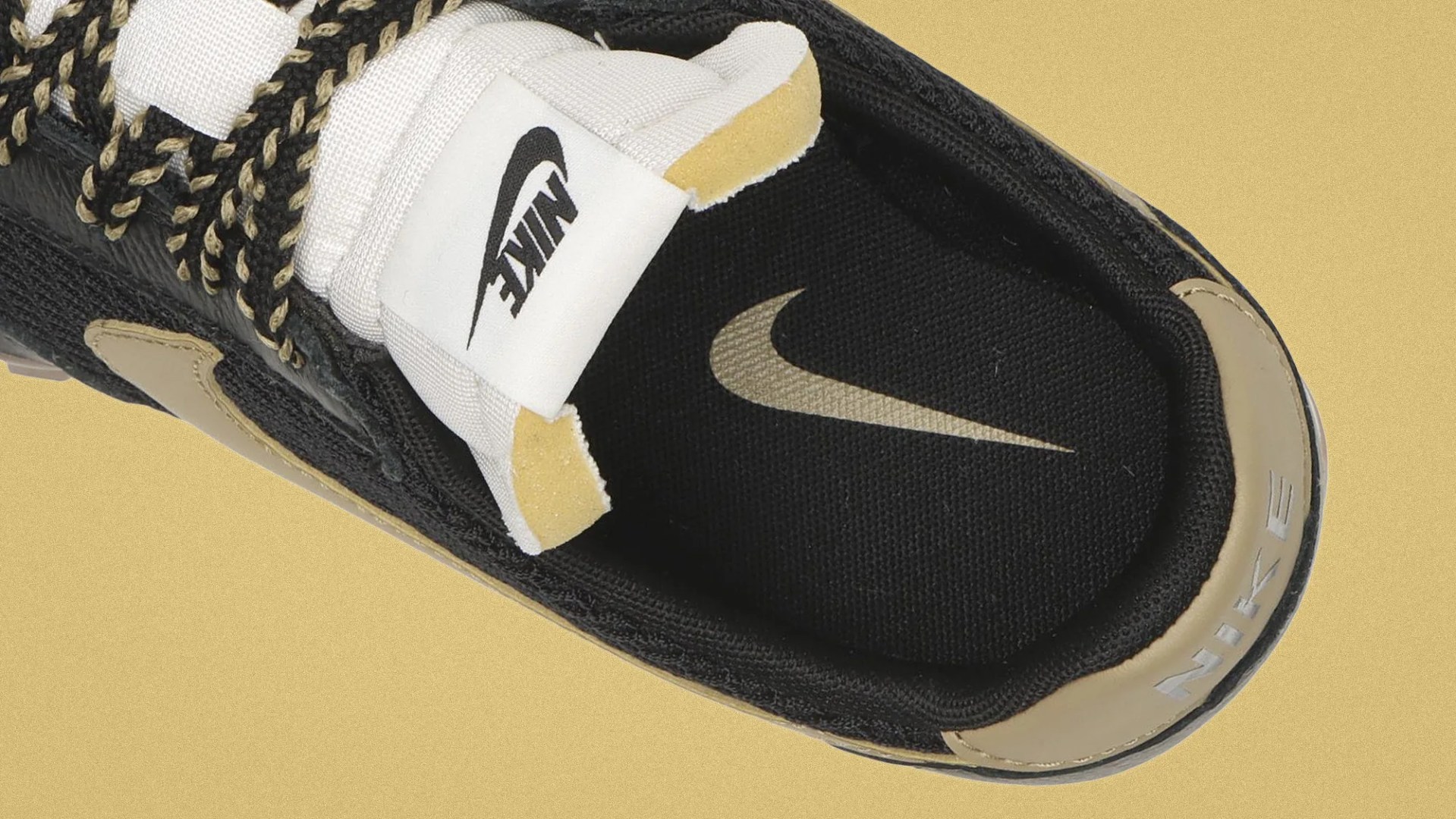 Top view of a black and beige Nike sneaker with black and beige braided laces and a white tongue label featuring the Nike logo.