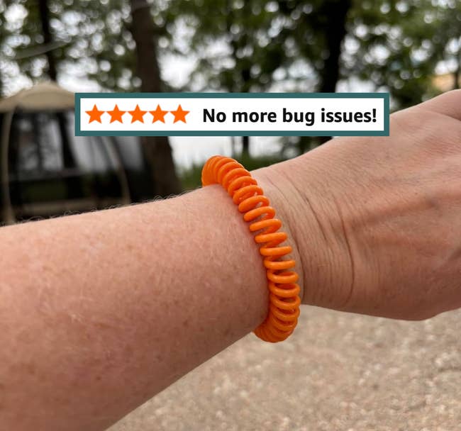 A person wearing a coiled bracelet outdoors, with trees in the background
