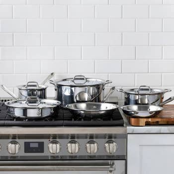 A set of stainless steel cookware displayed on a modern stove, featuring pots, pans, and lids for a kitchen-themed shopping article