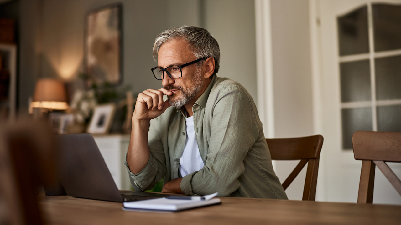 Discover a confident senior male freelancer reviewing his finances via an online document on a laptop