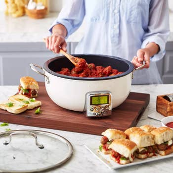 Person cooking meatballs in an electronic pot on a wooden board with sliders and lid nearby in a kitchen setting