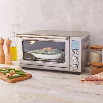 Countertop oven baking a dish with green beans and onions, surrounded by kitchen tools and ingredients