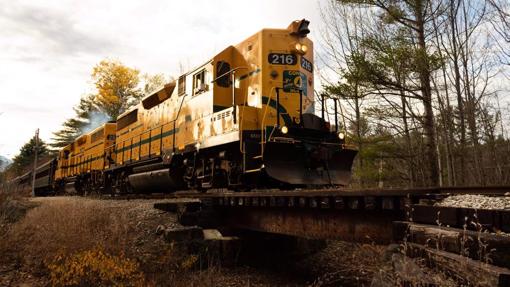 Bright yellow train, part of the Conway Scenic Railroad in North Conway, NH, under an overcast sky in the late autumn.