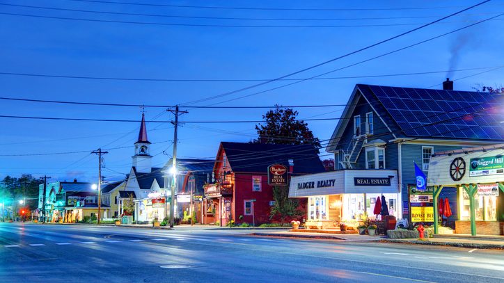 Downtown North Conway, New Hampshire at night, showing a church steeple, historic storefronts, and streetlights.