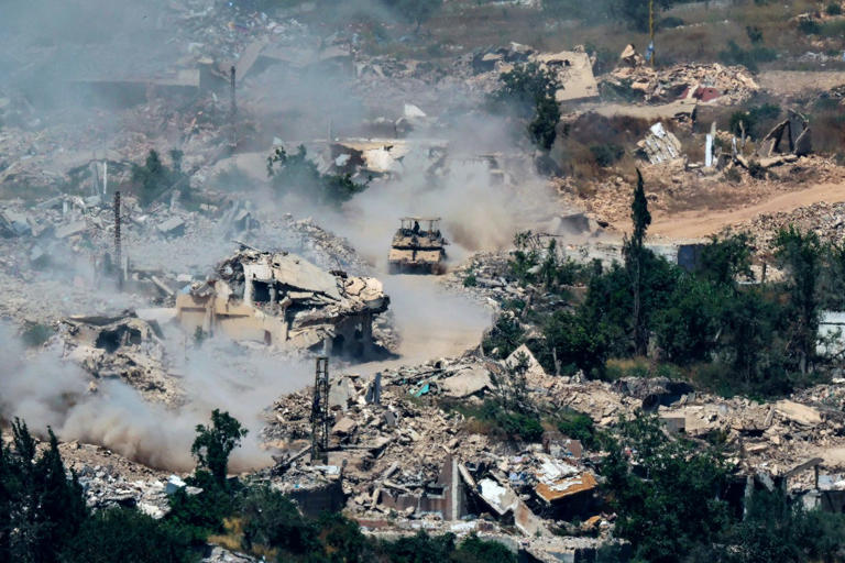Israeli tanks drive past destroyed buildings in southern Lebanon on Wednesday.