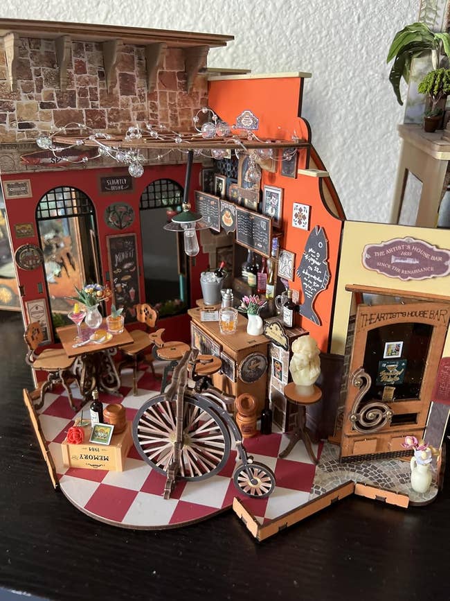 Detailed miniature café model with tables, chairs, and decorative signs, set in a cozy European style