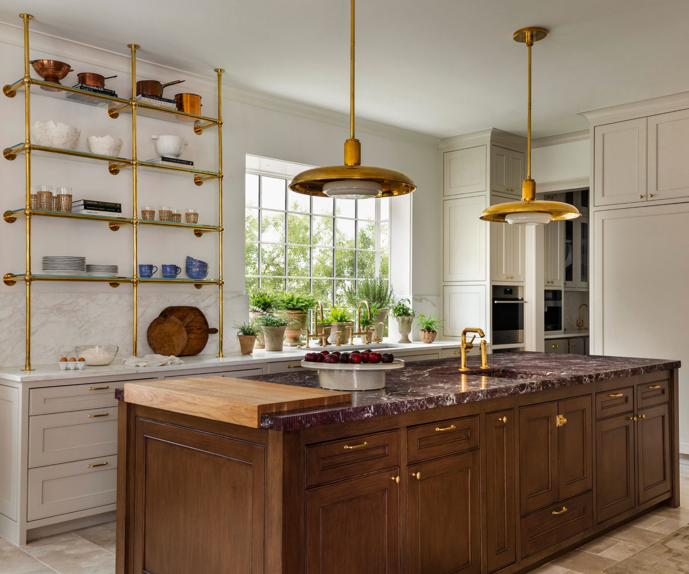 A kitchen with white perimeter cabinets and white countertops, paired with a wooden island topped with burgundy marble countertops and a wooden butcher block