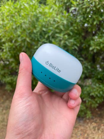 Hand holding a BioLite portable light device against a green leafy background