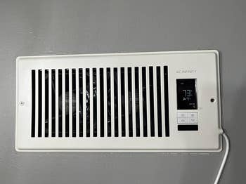 Wall-mounted electronic vent with a digital display showing 73°F, controlled by buttons on the side