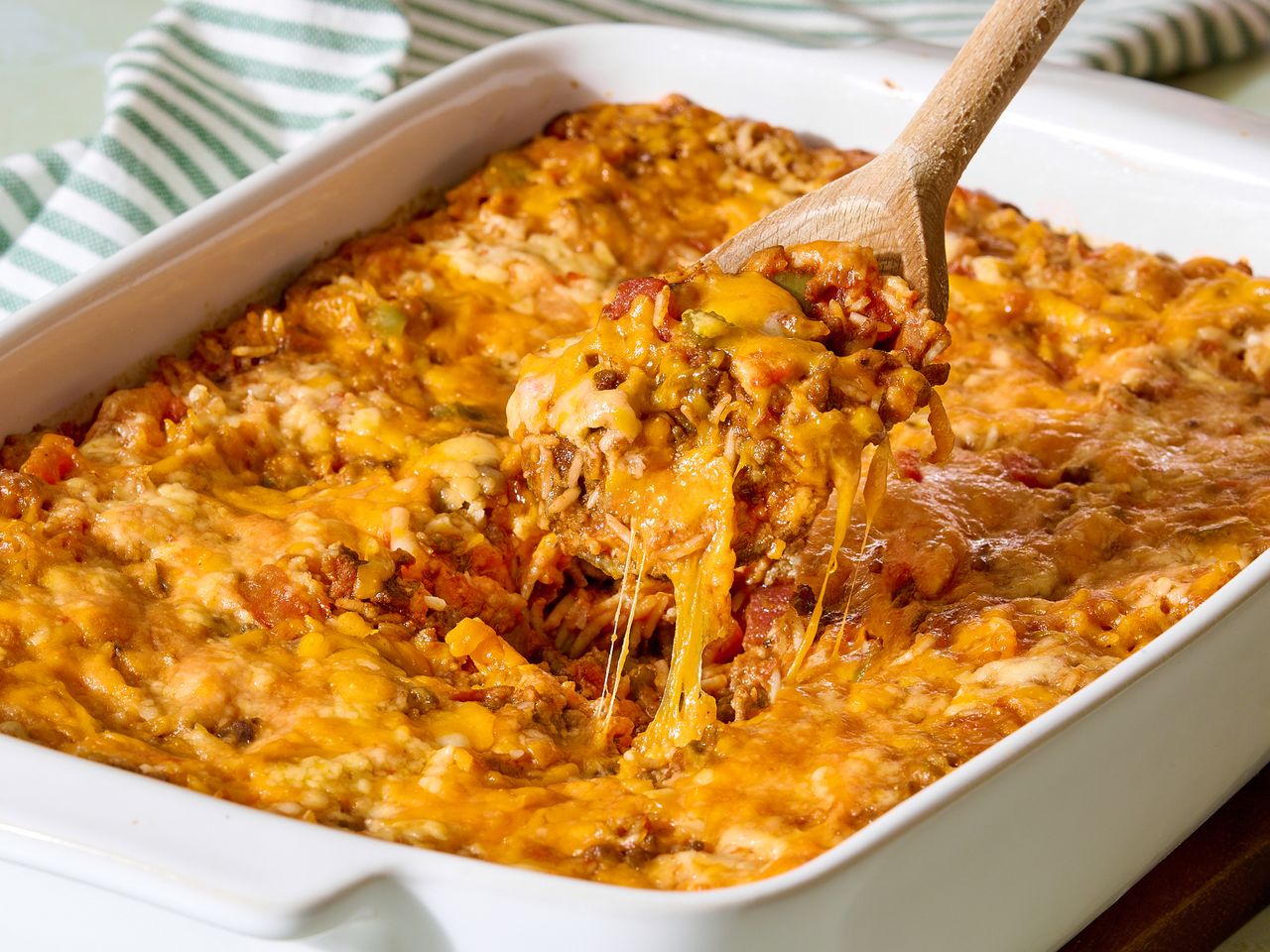 A baked stuffed pepper casserole being served with a wooden spoon