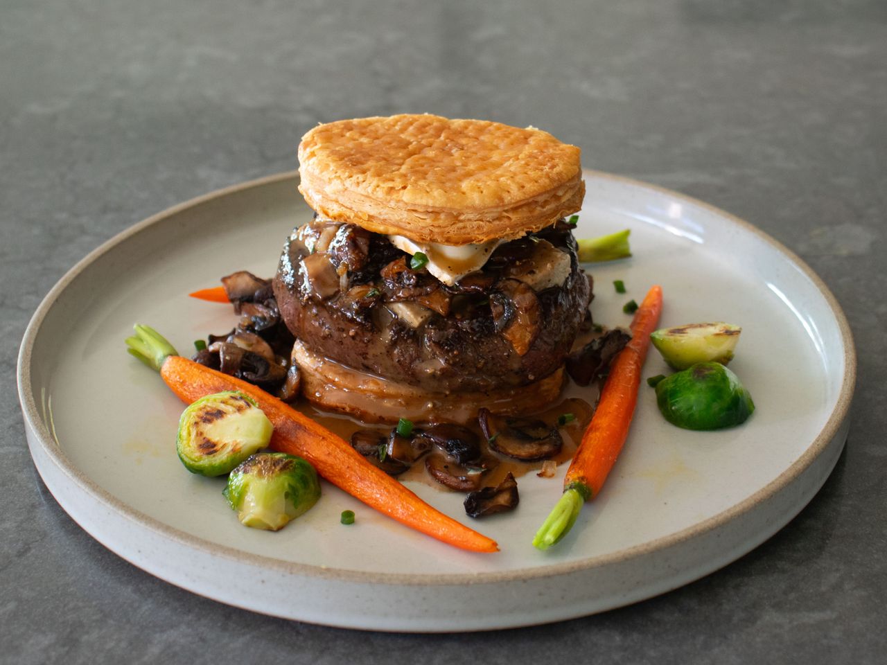 stacked deconstructed beef Wellington for one with vegetables on a rimmed plate