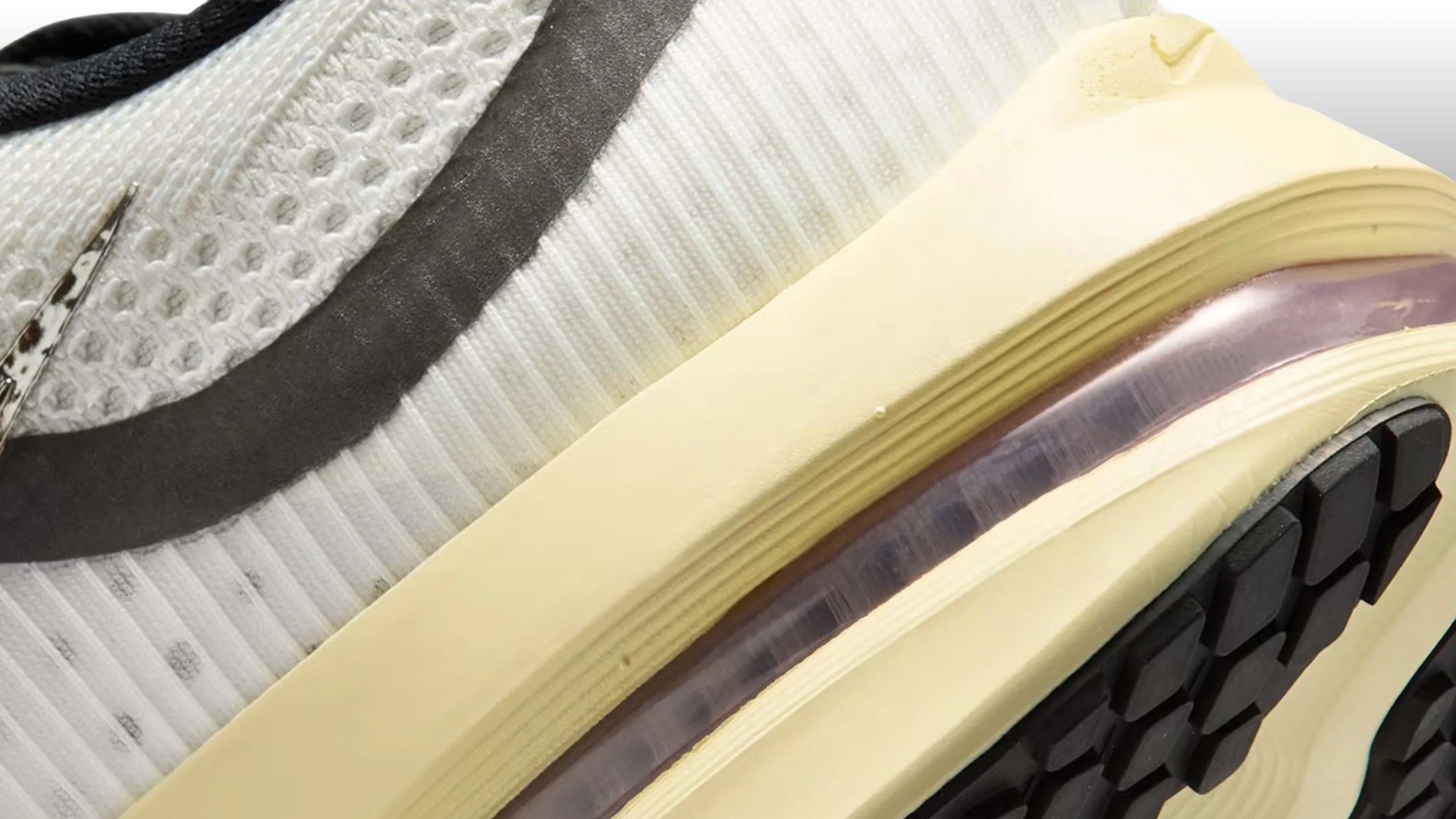 Close-up of a white and beige sneaker with a black sole and a transparent air cushion in the midsole.
