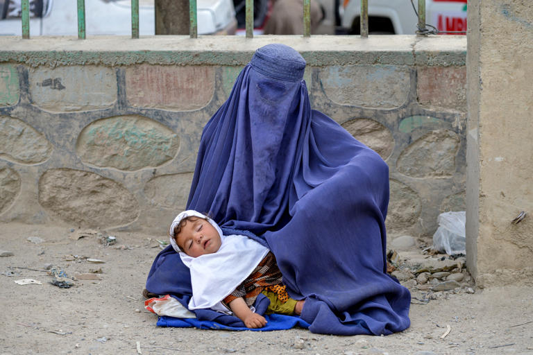 An Afghan burqa-clad woman carrying a child seeks alms along a road (AFP/Getty)