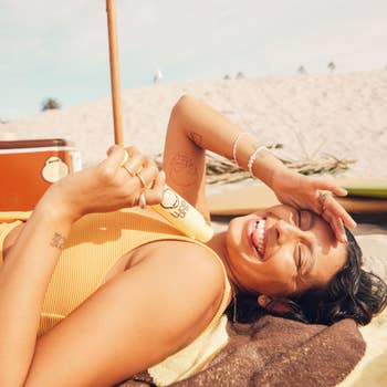Model smiling while lying on the beach, holding a popsicle, with tattoos and casual beachwear