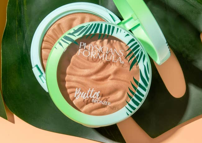 Physicians Formula Butter Bronzer compact open on a green leaf, showing the embossed bronzer surface
