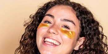 Smiling person with curly hair wearing gold under-eye patches for skincare