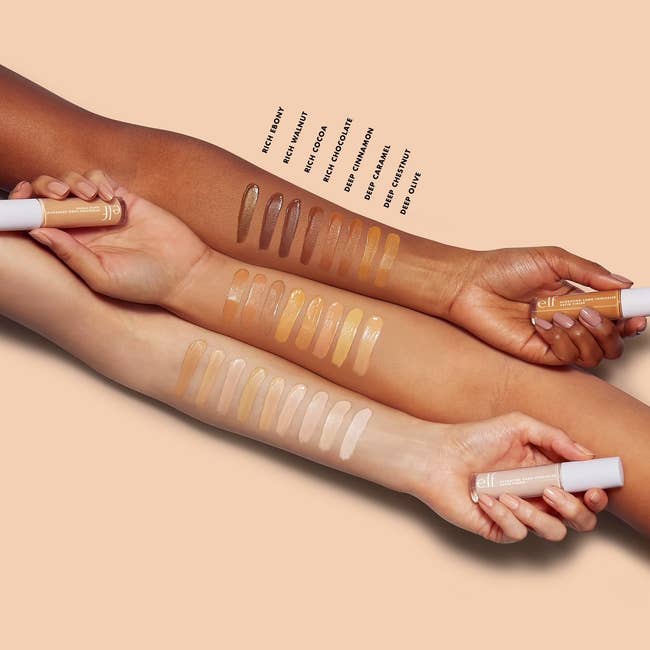Four arms displaying a range of concealer shades from light to dark, showing skin tone inclusivity. Tubes marked with different shade names