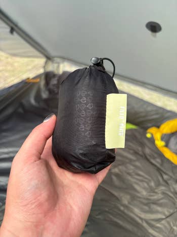 Hand holding a compact, black sleeping bag in a tent, labeled