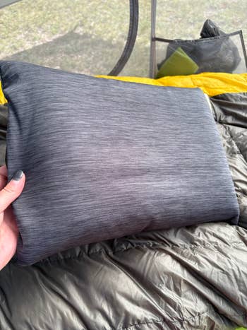 Person holding a rectangular camping pillow inside a tent, with a sleeping bag visible underneath