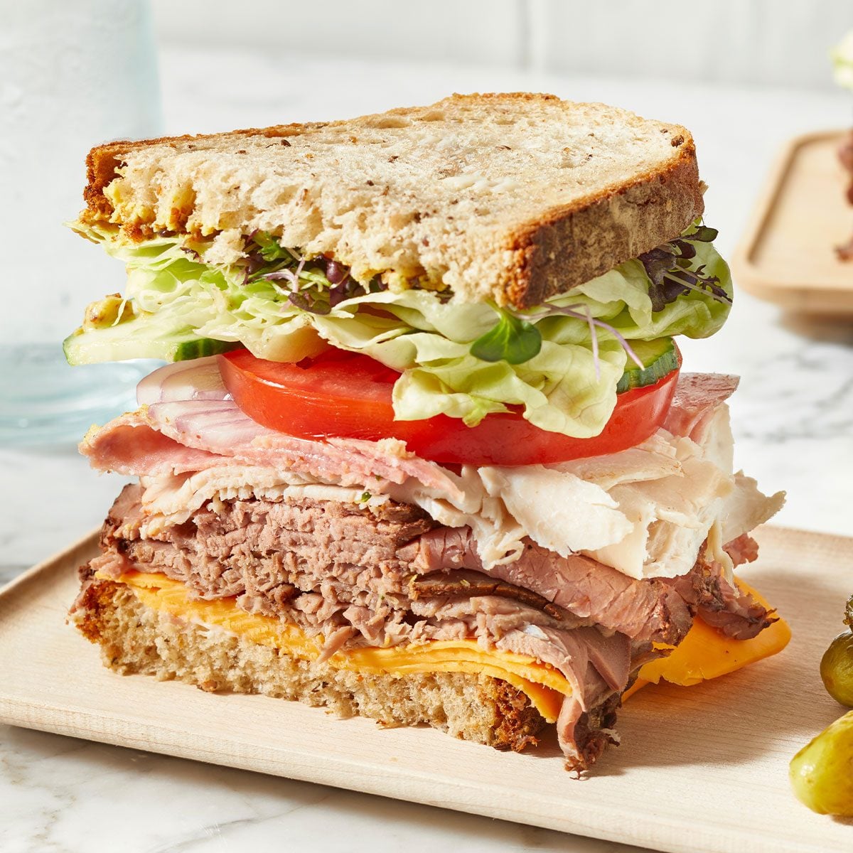 A loaded sandwich with a lot of greens, meat and cheese.