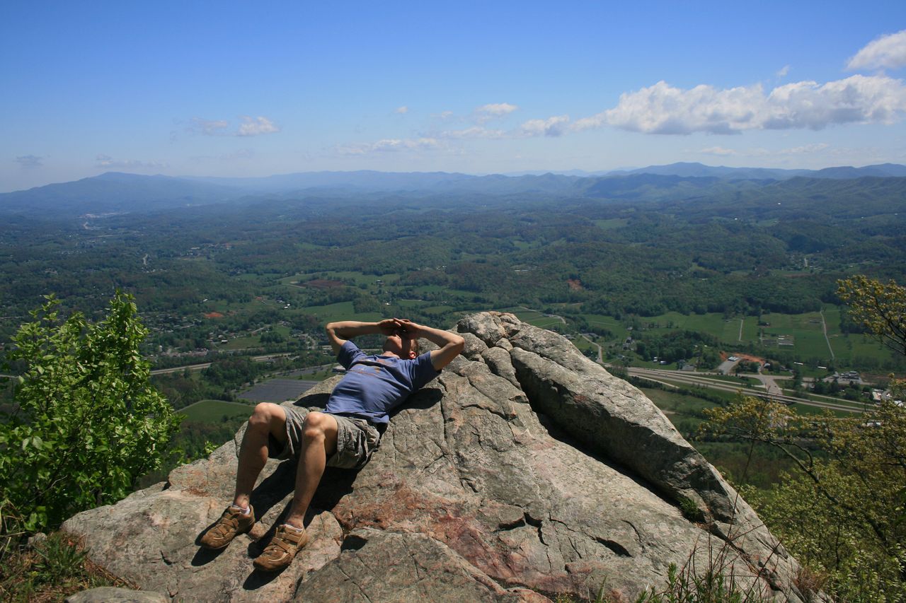 A person reclining on a rock overlooking a vast landscape with hills and trees
