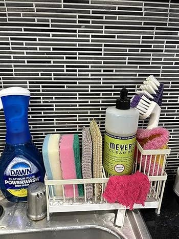 Kitchen sink with various cleaning supplies, including sponges, scrub brushes, and soap bottles organized in a caddy