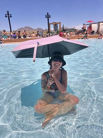 Reviewer sitting in a pool sitting in the shade of a pink parasol