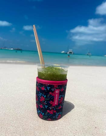 A slushee drink held in a floral JavaSok on the beach