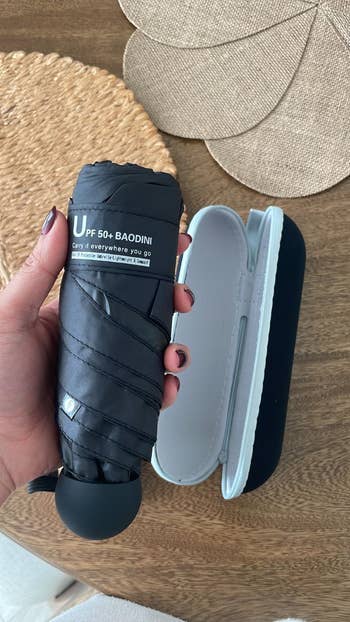 Reviewer holding a black parasol which is about the size of their hand with the hard cover case behind them