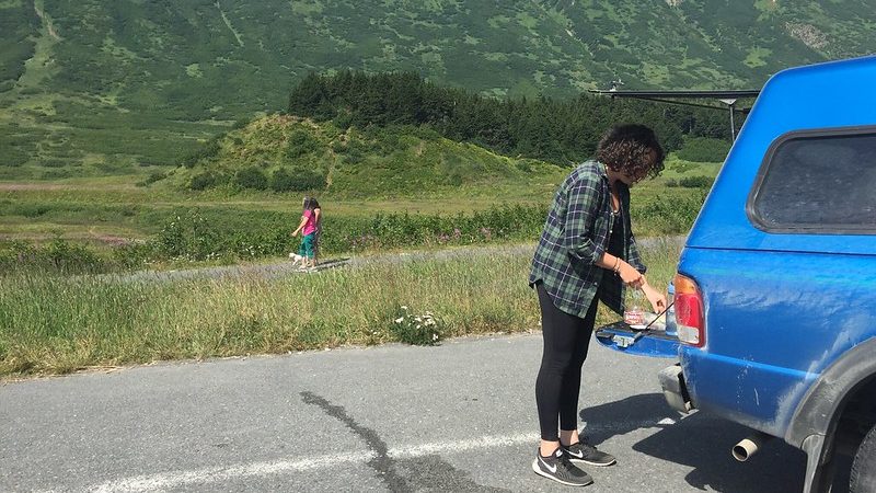 A woman opens the bed of her blue truck at a scenic rest stop in Alaska.