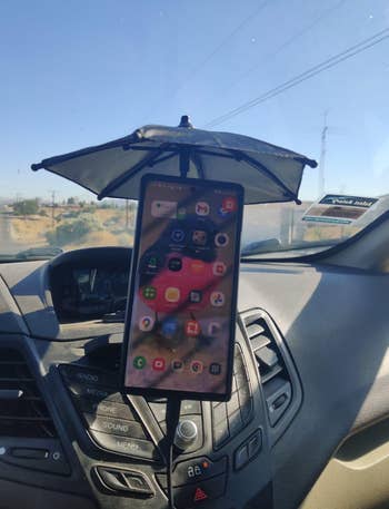 Phone mounted in a car with a small protective umbrella covering it, displaying app icons on the screen