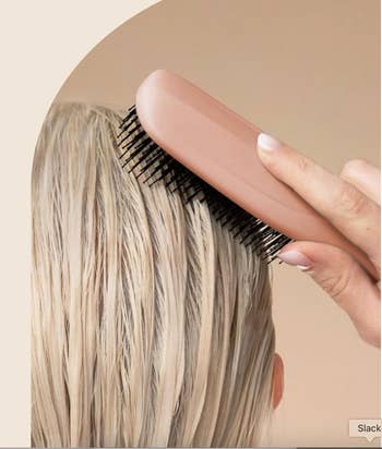 A hand holding a hairbrush, gently brushing through wet hair, illustrating hair care or styling