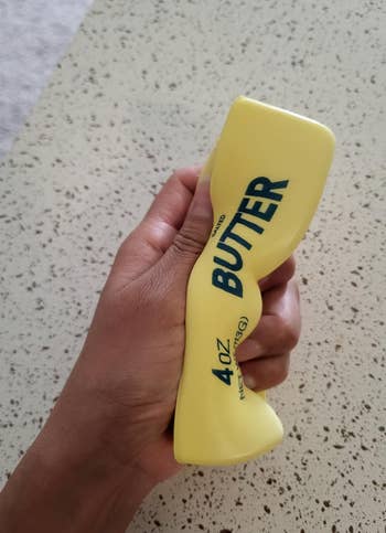 Hand squeezing a stress ball shaped like a butter stick, labeled
