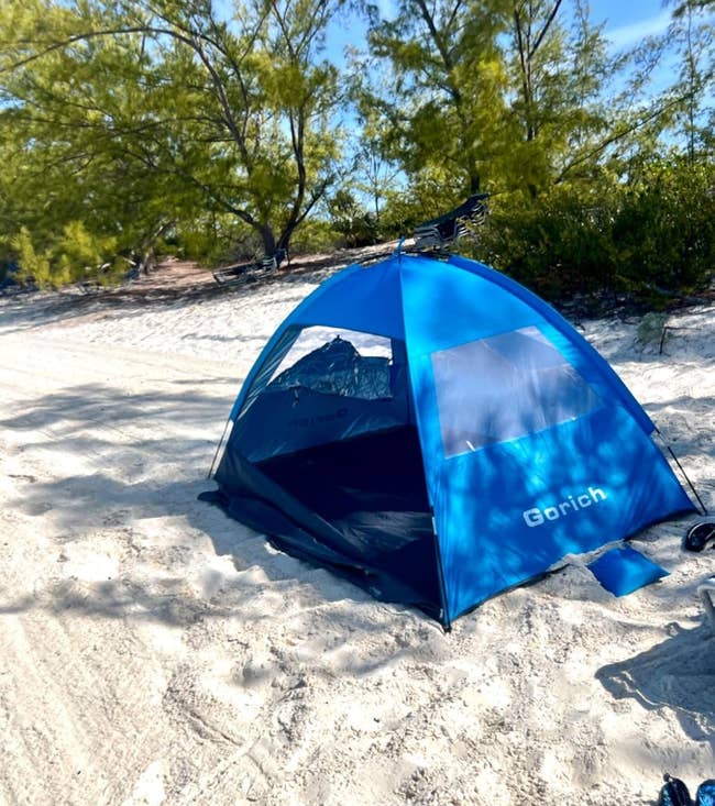 Beach tent set up on sand under trees, offering shade and protection