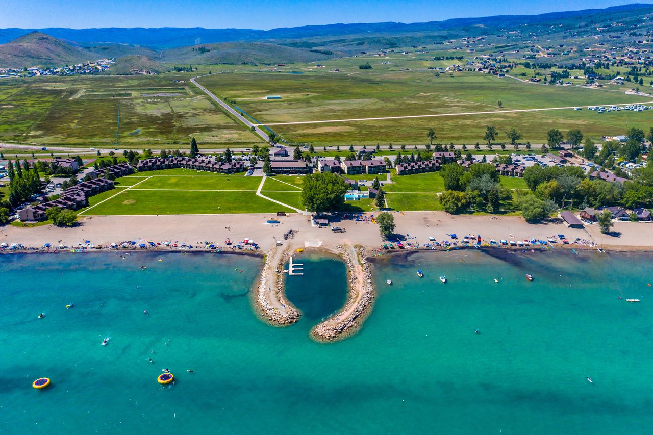 Aerial view of a beach breakwater and a dock extending into a lake with surrounding grassy and builtup areas