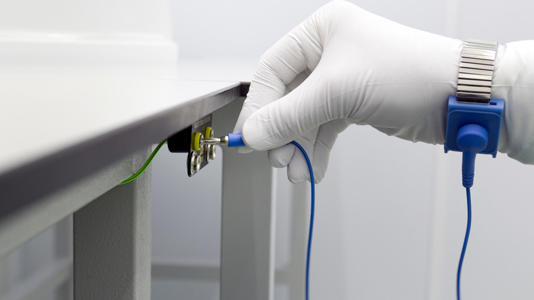A white gloved hand connecting an anti-static wrist strap to a ground source.