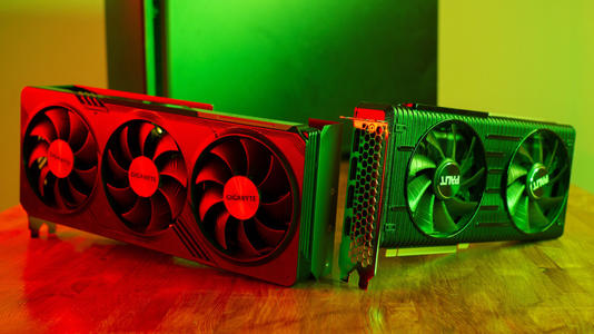 Two modern graphics cards displayed side by side on a desk under colored lighting.