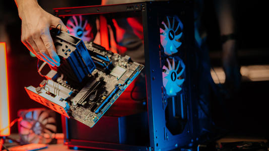 A person installing a motherboard with a large CPU cooler into a desktop PC case.