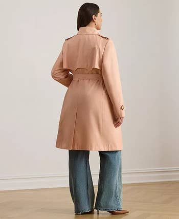 Person wearing a stylish trench coat and wide-leg jeans, standing in a minimalistic interior setting