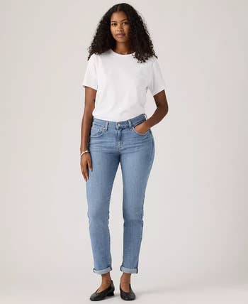 Person modeling casual outfit: white t-shirt, blue jeans, and black shoes, standing with one hand in pocket