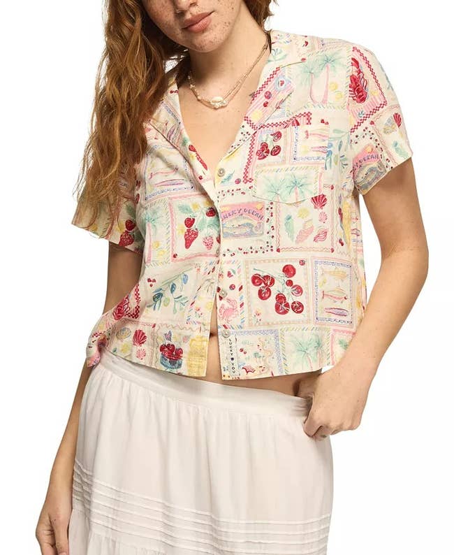 Person wearing a patterned short-sleeve button-up shirt and a white skirt, showcasing a casual, light, summery style ideal for casual outings